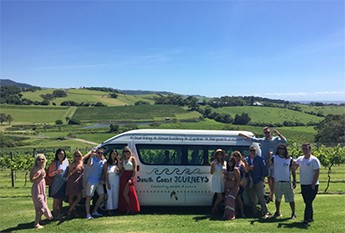 A dozen people posing with the bus in front of rolling meadows bathed in sunshine